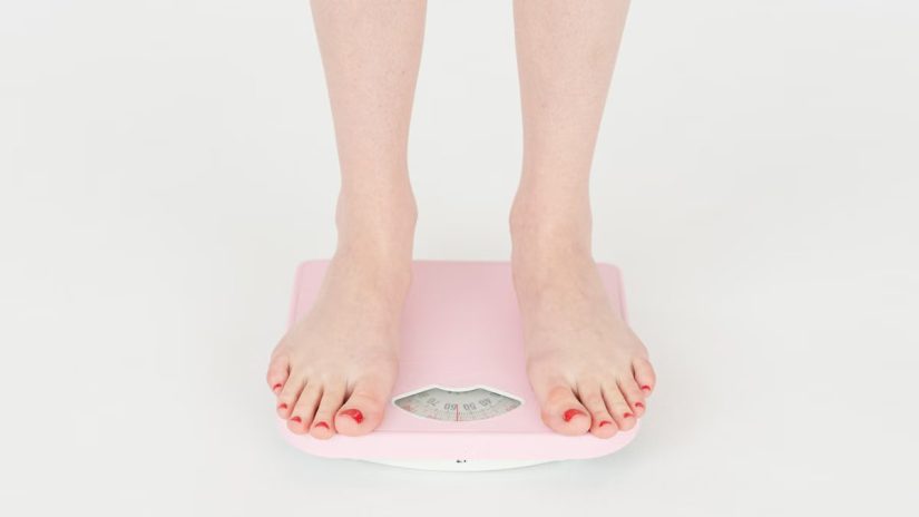 High angle of crop anonymous female measuring weight for control body against white background in studio
